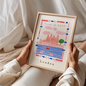 Puede incluir: Una ilustraci&oacute;n enmarcada de la Torre de Londres, un castillo rosa con agua azul y flamencos rosas. La ilustraci&oacute;n est&aacute; rodeada por un borde colorido con flores, c&iacute;rculos y rayas. El texto "Tower of London" y "London" est&aacute; escrito en azul y rojo. La firma del artista est&aacute; en la esquina inferior derecha.