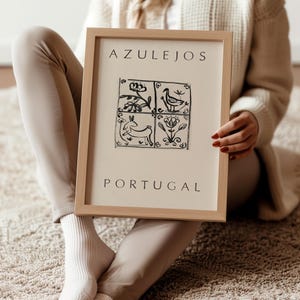 May include: A framed print with the text "AZULEJOS PORTUGAL" and a black and white illustration of four tiles with stylized designs of a bird, flowers, and a rabbit.
