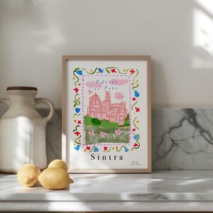 May include: A framed print of a pink castle with a blue sky and white clouds. The castle is surrounded by green trees and flowers. The text "Palacio de Pena" and "Sintra" are printed below the image.