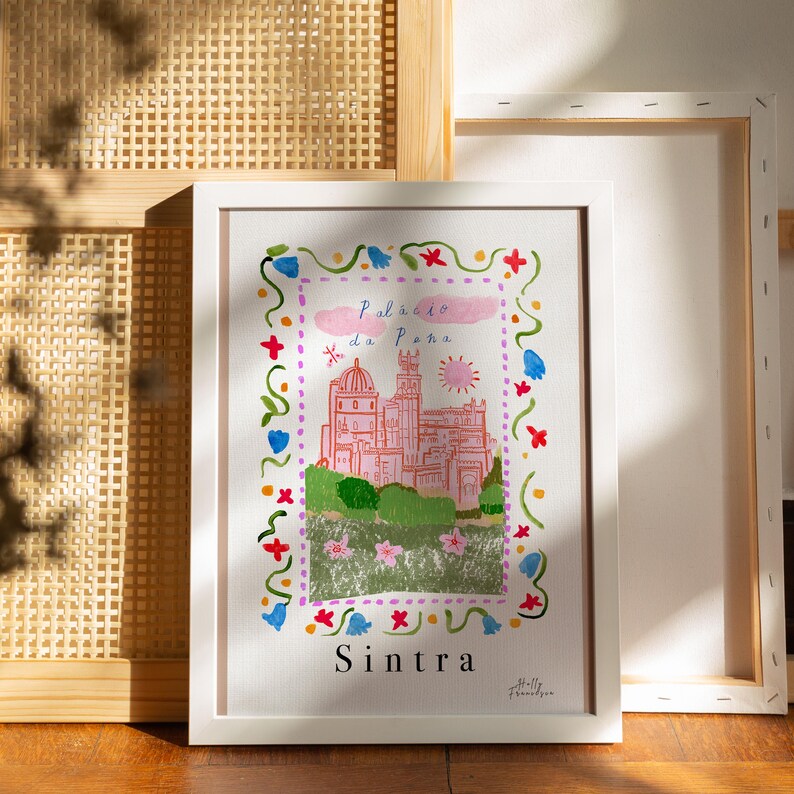 May include: A white framed print with a colorful illustration of a pink castle with a blue sky and sun. The text "Pal&aacute;cio da Pena" and "Sintra" are written in black below the castle.