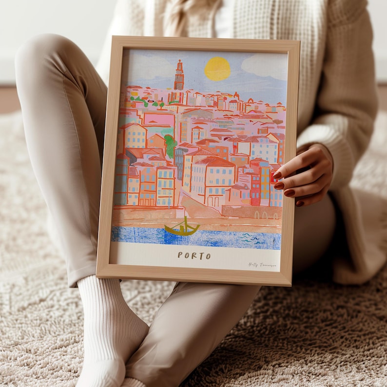May include: A framed illustration of the city of Porto, Portugal. The illustration is done in a colorful, whimsical style with a bright yellow sun in the sky. The text "PORTO" is printed at the bottom of the illustration.