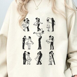 May include: Cream-colored sweatshirt featuring a repeating black and white graphic of couples dancing. The illustrations depict various dance poses, including lifts and embraces. The design is simple and elegant, suitable for casual wear.