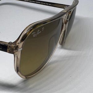 May include: Aviator sunglasses with a translucent beige frame and brown polarised lenses. The right lens features the white Ray-Ban P logo. The inner temple is printed with the text RB 2309 BILL ONE 1282/W0 57 18 145 3P.