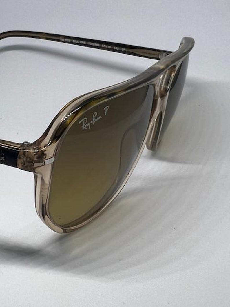 May include: Aviator sunglasses with a translucent beige frame and brown polarised lenses. The right lens features the white Ray-Ban P logo. The inner temple is printed with the text RB 2309 BILL ONE 1282/W0 57 18 145 3P.