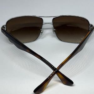 Pode incluir: &Oacute;culos de sol estilo aviador com arma&ccedil;&atilde;o de metal prateado e lentes degrad&ecirc; castanhas. As hastes s&atilde;o feitas de material com padr&atilde;o de tartaruga castanho. O log&oacute;tipo Ray-Ban &eacute; vis&iacute;vel na lente direita e no lado exterior de ambas as hastes.