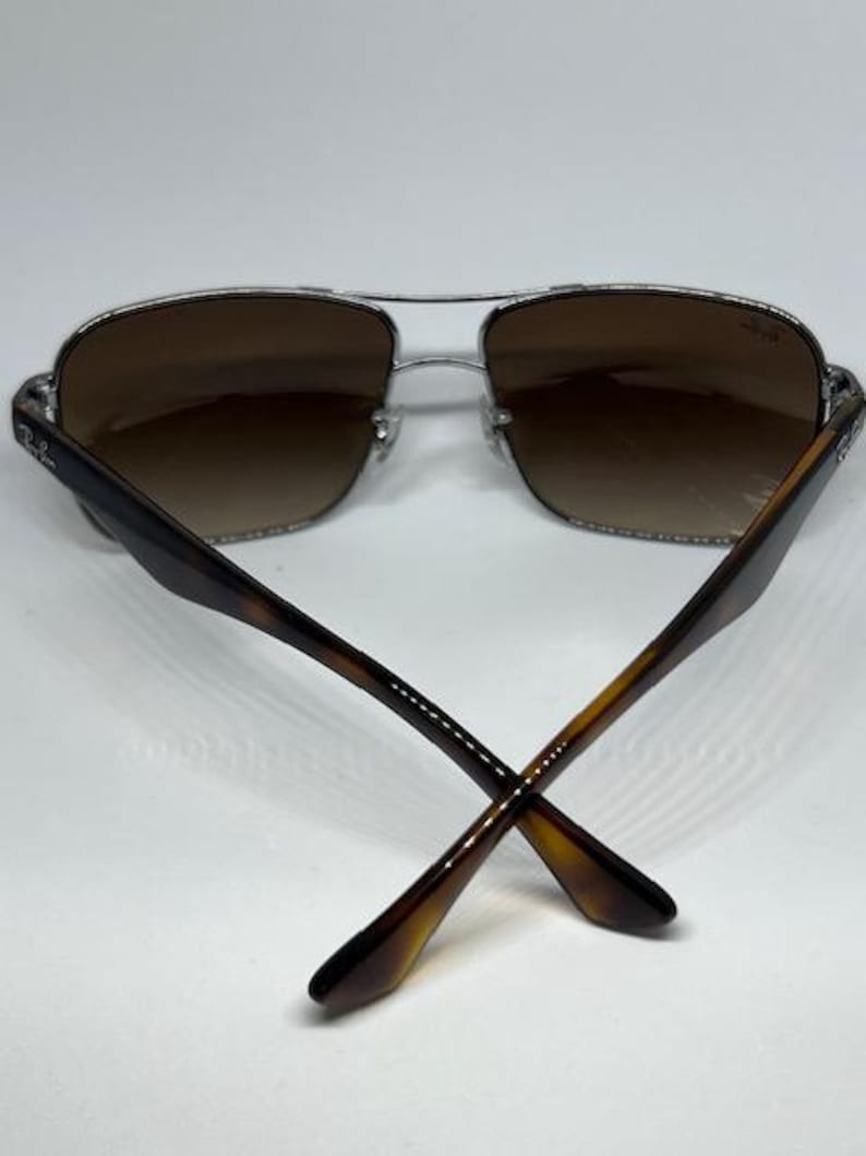 Pode incluir: &Oacute;culos de sol estilo aviador com arma&ccedil;&atilde;o de metal prateado e lentes degrad&ecirc; castanhas. As hastes s&atilde;o feitas de material com padr&atilde;o de tartaruga castanho. O log&oacute;tipo Ray-Ban &eacute; vis&iacute;vel na lente direita e no lado exterior de ambas as hastes.