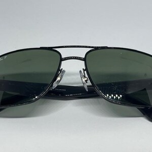 May include: Black aviator sunglasses with a double bridge design and dark green polarized lenses. The left lens features the Ray-Ban P logo in white. The frames are constructed with thin black metal rims and black plastic temple arms.