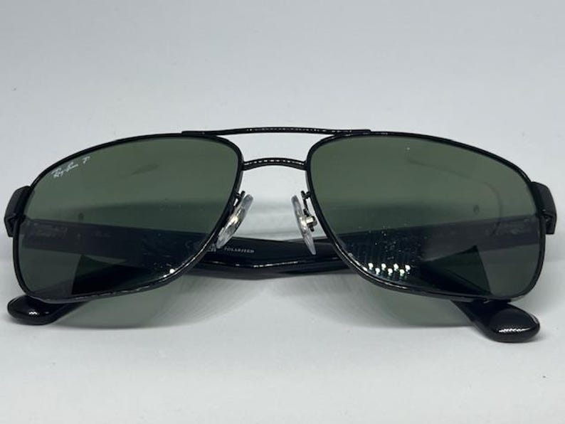 May include: Black aviator sunglasses with a double bridge design and dark green polarized lenses. The left lens features the Ray-Ban P logo in white. The frames are constructed with thin black metal rims and black plastic temple arms.