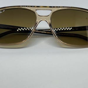 May include: Ray-Ban polarised sunglasses featuring a translucent beige plastic frame with a double bridge design and brown tinted lenses. The left lens displays the white Ray-Ban P logo, and the temples are dark brown with a tortoiseshell pattern.
