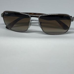 Pode incluir: &Oacute;culos de sol Ray-Ban com arma&ccedil;&atilde;o de metal prateado de formato retangular e lentes degrad&ecirc; castanhas. A lente esquerda apresenta o log&oacute;tipo Ray-Ban em branco. As hastes t&ecirc;m um padr&atilde;o de tartaruga em castanho escuro.