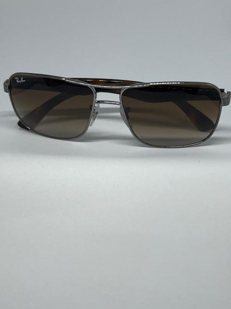 Pode incluir: &Oacute;culos de sol Ray-Ban com arma&ccedil;&atilde;o de metal prateado de formato retangular e lentes degrad&ecirc; castanhas. A lente esquerda apresenta o log&oacute;tipo Ray-Ban em branco. As hastes t&ecirc;m um padr&atilde;o de tartaruga em castanho escuro.