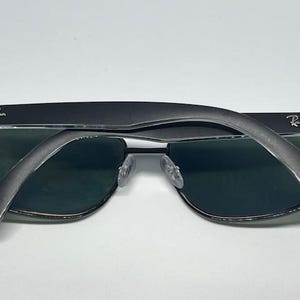 May include: Black Ray-Ban sunglasses featuring dark green lenses and a matte black frame. The temples are folded over the front of the frames, displaying the silver Ray-Ban logo on both the left and right sides of the temple arms.
