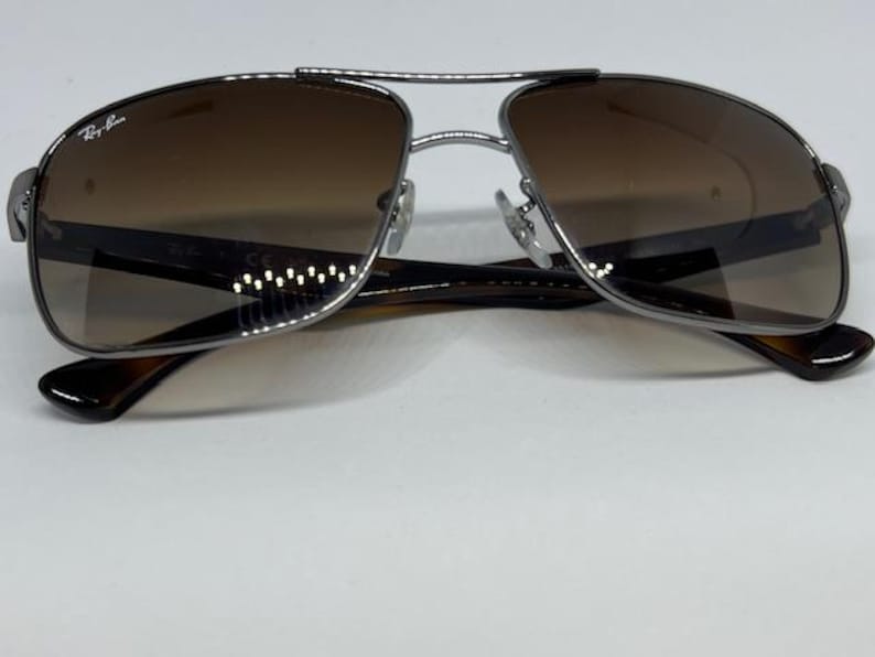 Pode incluir: &Oacute;culos de sol aviador Ray-Ban com uma arma&ccedil;&atilde;o fina em metal prateado gunmetal e design de ponte dupla. As lentes t&ecirc;m um tom castanho degrad&ecirc; e as hastes s&atilde;o feitas de um material castanho escuro com padr&atilde;o de tartaruga e dobradi&ccedil;as.