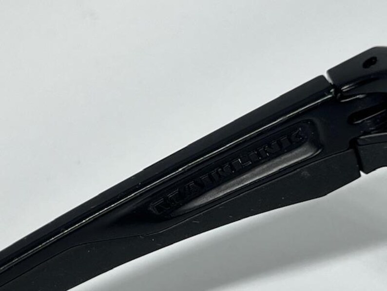 May include: A matte black plastic component with a hinged section and a recessed area featuring the embossed text "RAWLINGS". The object has a smooth, angular design with a visible pivot point and a clean, uniform dark finish throughout the piece.