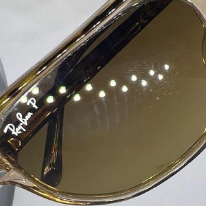 May include: Tortoiseshell-patterned sunglasses with brown lenses. The left lens features the white Ray-Ban P logo. The frame has a glossy finish, and the temple arm is visible through the lens, showing the Ray-Ban branding and polarised text.