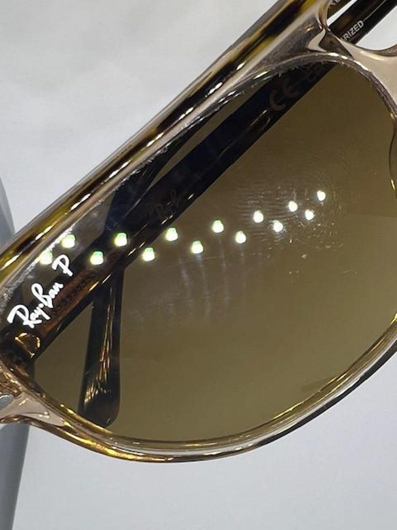 May include: Tortoiseshell-patterned sunglasses with brown lenses. The left lens features the white Ray-Ban P logo. The frame has a glossy finish, and the temple arm is visible through the lens, showing the Ray-Ban branding and polarised text.