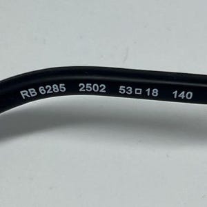 Puede incluir: Una patilla de gafas negra con texto impreso en blanco en el lado interior. El texto dice RB 6285 2502 53 18 140, indicando el n&uacute;mero de modelo, c&oacute;digo de color, ancho de lente, ancho de puente y longitud de patilla en mil&iacute;metros.