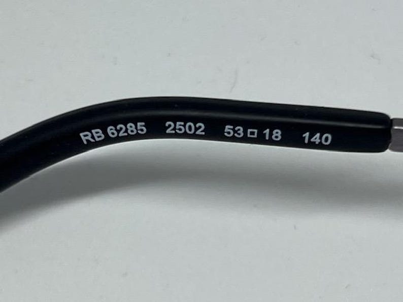 Puede incluir: Una patilla de gafas negra con texto impreso en blanco en el lado interior. El texto dice RB 6285 2502 53 18 140, indicando el n&uacute;mero de modelo, c&oacute;digo de color, ancho de lente, ancho de puente y longitud de patilla en mil&iacute;metros.