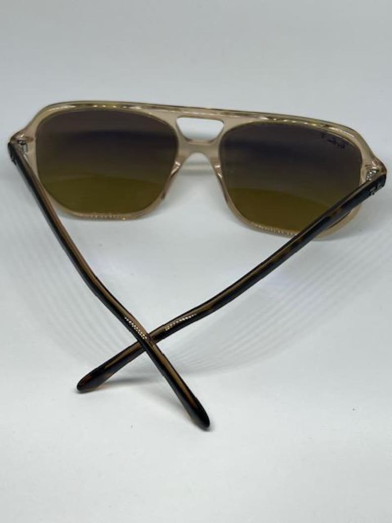 May include: Aviator sunglasses featuring a translucent beige frame with a double bridge design. The lenses have a gradient brown tint, and the temples are crafted from a dark brown tortoiseshell pattern material with the Ray-Ban logo visible.