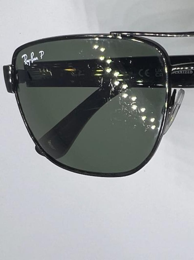 May include: Black metal frame sunglasses with dark green polarized lenses. The upper left lens features the white Ray-Ban P logo. The temple arm displays the CE mark and the word POLARIZED. The design includes a double bridge across the top.