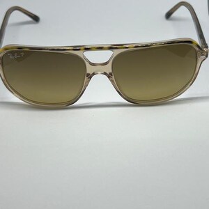 May include: Aviator sunglasses featuring a translucent beige frame with a tortoiseshell pattern along the top brow bar. The lenses are a solid brown tint, and the left lens displays the Ray-Ban P logo in white text on the upper corner.
