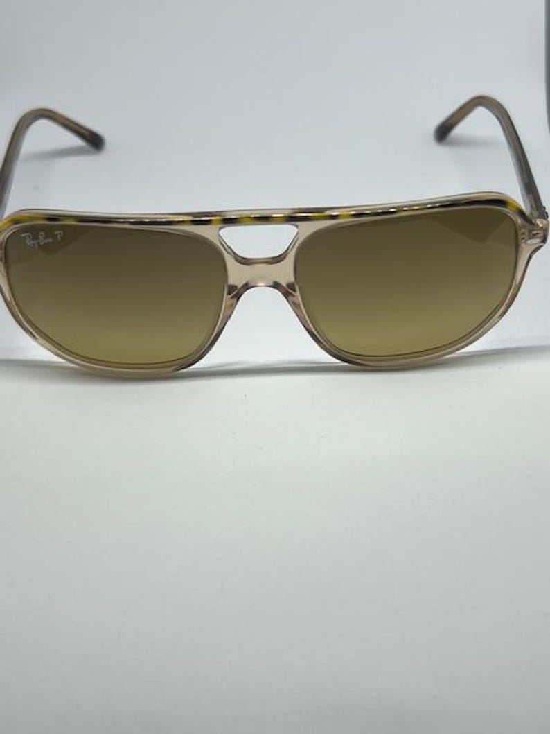 May include: Aviator sunglasses featuring a translucent beige frame with a tortoiseshell pattern along the top brow bar. The lenses are a solid brown tint, and the left lens displays the Ray-Ban P logo in white text on the upper corner.