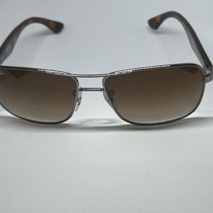 Pode incluir: &Oacute;culos de sol com uma arma&ccedil;&atilde;o fina de metal prateado e design de ponte dupla. As lentes s&atilde;o castanhas com um tom degrad&eacute;, mais escuro no topo e mais claro na parte inferior. As hastes apresentam um padr&atilde;o de tartaruga castanho e preto.