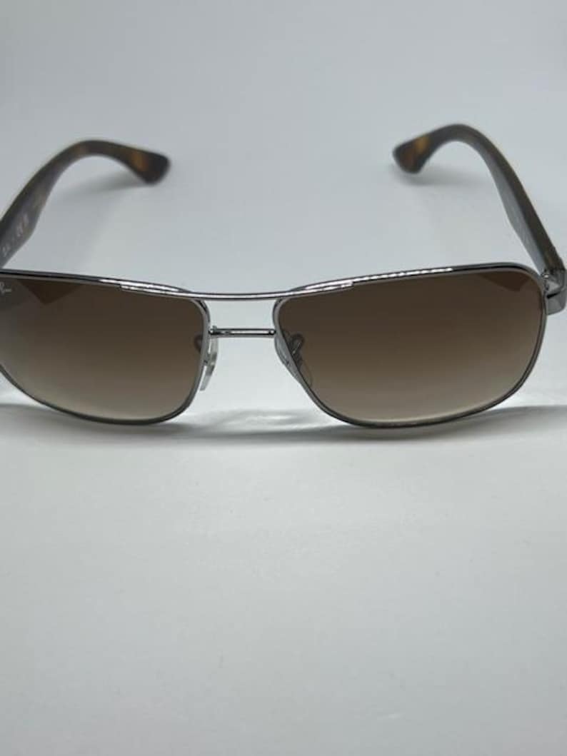 Pode incluir: &Oacute;culos de sol com uma arma&ccedil;&atilde;o fina de metal prateado e design de ponte dupla. As lentes s&atilde;o castanhas com um tom degrad&eacute;, mais escuro no topo e mais claro na parte inferior. As hastes apresentam um padr&atilde;o de tartaruga castanho e preto.