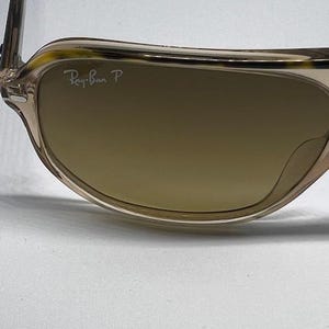 May include: Sunglasses with a translucent light brown frame featuring a tortoiseshell pattern along the top rim. The brown tinted lenses include the white Ray-Ban P logo printed in the upper corner, indicating polarised lens technology.