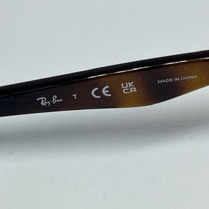 Pode incluir: Uma haste de &oacute;culos com padr&atilde;o de tartaruga castanho e preto, apresentando o texto impresso em branco Ray-Ban, a letra T, a marca CE, a marca UKCA e o texto MADE IN CHINA na superf&iacute;cie interior da haste.