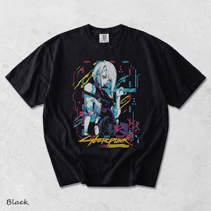 May include: A black short-sleeved t-shirt featuring a graphic print of a character with white hair. The design includes the text "LUCY" repeated in the background, along with "CYBERPUNK EDGERUNNERS" in yellow text at the bottom, accented by blue, pink, and yellow lines.