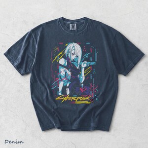 May include: A dark blue short-sleeve t-shirt featuring a graphic print of the character Lucy from Cyberpunk Edgerunners. The design includes the text "LUCY" repeated in a digital font, alongside yellow, pink, and blue abstract geometric lines.