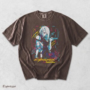 May include: An espresso-coloured short-sleeve t-shirt featuring a graphic print of the character Lucy from Cyberpunk Edgerunners. The design includes neon blue, pink, and yellow accents with the text Cyberpunk Edgerunners and the name Lucy.