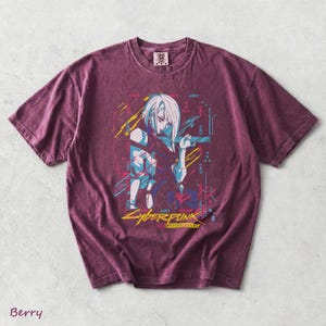 May include: A berry-coloured short-sleeve t-shirt featuring a graphic print of an anime character with white hair. The design includes the text "LUCY" repeated, "CYBERPUNK" in yellow, and "EDGERUNNERS" in a smaller font, accented with blue and yellow lines.
