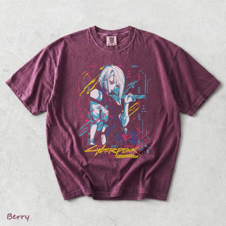 May include: A berry-coloured short-sleeve t-shirt featuring a graphic print of an anime character with white hair. The design includes the text "LUCY" repeated, "CYBERPUNK" in yellow, and "EDGERUNNERS" in a smaller font, accented with blue and yellow lines.