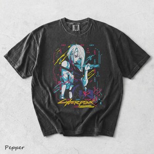 May include: A charcoal grey short-sleeve t-shirt featuring a graphic print of the character Lucy from Cyberpunk Edgerunners. The design includes neon blue, pink, and yellow accents with the text Cyberpunk Edgerunners and the name Lucy repeated.