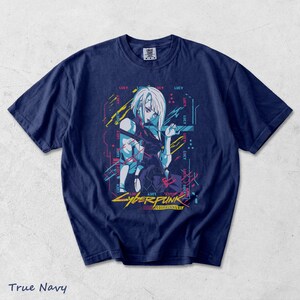 May include: A true navy blue short-sleeve t-shirt featuring a graphic print of the character Lucy from Cyberpunk Edgerunners. The design includes neon-coloured abstract lines, the repeated text Lucy, and the Cyberpunk Edgerunners logo in yellow.