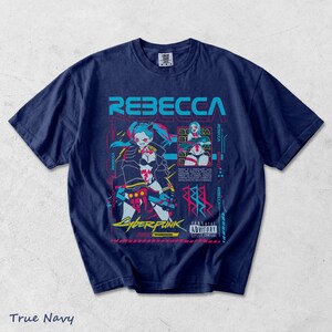 K&ouml;nnte beinhalten: Ein marineblaues T-Shirt mit einem Grafikdruck der Figur Rebecca aus Cyberpunk Edgerunners. Das Design zeigt den Namen REBECCA in gro&szlig;en cyanfarbenen Buchstaben, ein kleineres eingef&uuml;gtes Bild, japanischen Text und ein Parental Advisory Etikett.