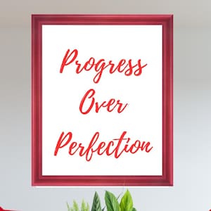 Puede incluir: Una pieza de arte mural rectangular en un marco rojo con el texto rojo Progress Over Perfection sobre un fondo blanco, flanqueada por dos sillones rojos con patas de madera clara y una jardinera de madera llena de follaje verde.