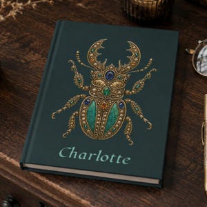 May include: A dark teal hardcover journal featuring a central illustration of a stag beetle adorned with gold, blue, green, and amber-colored jewel accents. The name Charlotte is printed in a light teal serif font below the beetle illustration.