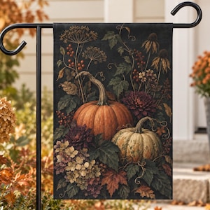 May include: A rectangular garden flag featuring a dark background with a botanical arrangement of two pumpkins, deep red dahlias, dried hydrangea clusters, autumn leaves, and berry sprigs, all displayed on a black metal garden flag stand.
