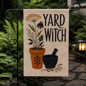 Könnte beinhalten: Eine rechteckige Gartenflagge mit beigem Hintergrund und dem schwarzen Schriftzug YARD WITCH. Das Motiv zeigt einen terrakottafarbenen Topf mit einer hohen Pflanze mit gelben und dunklen Blüten sowie einen schwarzen Mörser mit Stößel.