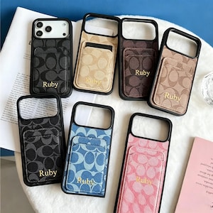 May include: A collection of seven rectangular phone cases with black frames, each featuring a card holder pocket on the back. The cases display various colors including black, beige, brown, tan, blue, and pink, all with a repeating logo pattern and the name Ruby printed in gold lettering.