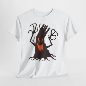 May include: A white short-sleeved t-shirt featuring a central graphic of a dark brown, gnarled tree with jagged, claw-like branches. The tree has a menacing face with glowing orange eyes and a sharp, jagged orange mouth set against the dark trunk.
