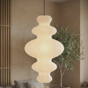Może przedstawiać: Kremowa papierowa lampa wisząca o wielopoziomowym, organicznym, pękatym kształcie. Oprawa oświetleniowa posiada delikatną, prążkowaną fakturę na całej powierzchni i jest zawieszona na cienkim czarnym przewodzie, emitując miękkie, rozproszone światło.