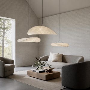 May include: Three suspended pendant lights with curved, off-white, textured shades hanging at varying heights. The fixtures feature thin black cords and emit a soft, diffused glow, illuminating the space below with a warm, ambient light.