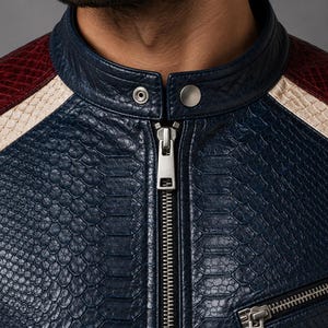 May include: A jacket featuring a textured, snakeskin-patterned finish in deep navy blue. The garment includes a mandarin collar with a silver-toned snap button closure, a central metal zipper, and contrasting cream and dark red shoulder panels.