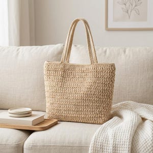 Puede incluir: Un bolso tote de color beige elaborado con un patrón de punto de ganchillo texturizado. El bolso cuenta con dos asas verticales a juego unidas al borde superior, una base rectangular y un color tostado claro uniforme en toda la estructura.