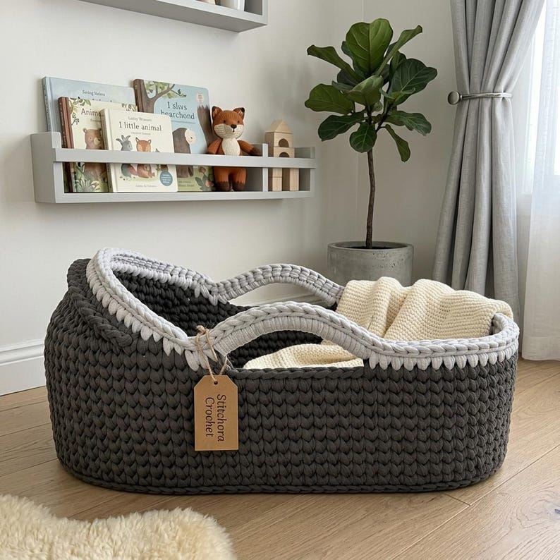 Peut inclure: Un panier ovale en crochet gris fonc&eacute; avec un bord gris clair et deux anses assorties. Une couverture en tricot cr&egrave;me est rang&eacute;e &agrave; l'int&eacute;rieur. Une &eacute;tiquette rectangulaire en papier brun attach&eacute;e &agrave; l'anse porte le texte Stitchora Crochet.