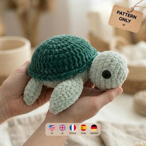 Puede incluir: Una tortuga de peluche tejida a ganchillo con un caparazón verde oscuro y cabeza y aletas de color verde menta claro. La tortuga tiene un ojo de plástico negro visible. Una etiqueta rectangular beige indica PATTERN ONLY con un corazón.